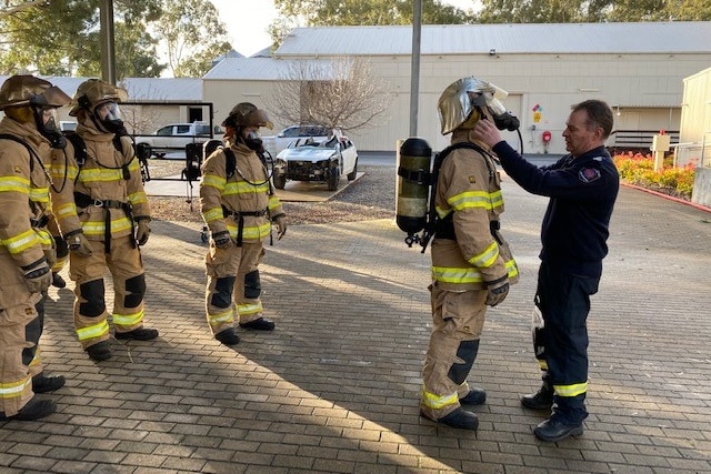 A man wearing blue looks at firefighters in uniform in an undercover paved area 