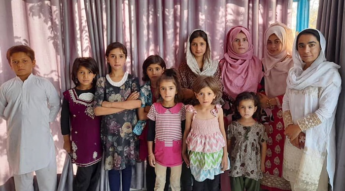 A group shot shows eight children and three women in traditional Afghan dress. 