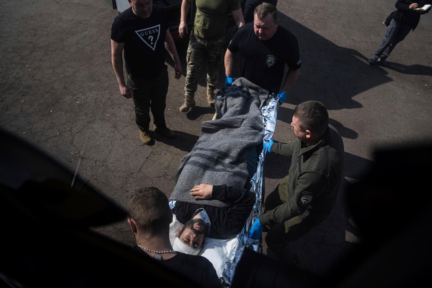A man lays on a stretcher surrounded by volunteers.