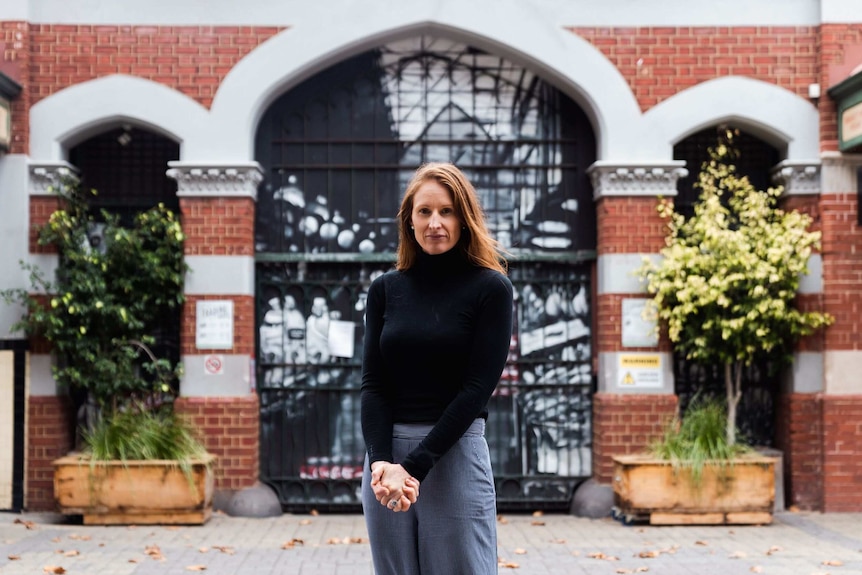 Woman stands outside closed gate of building