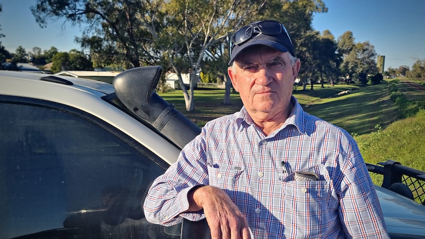 Man standing near a car wearing blue shirt and cap.