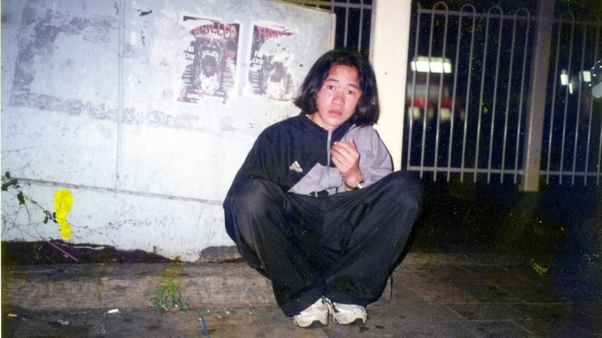 Teenage boy sitting on curb outside of train station at night.