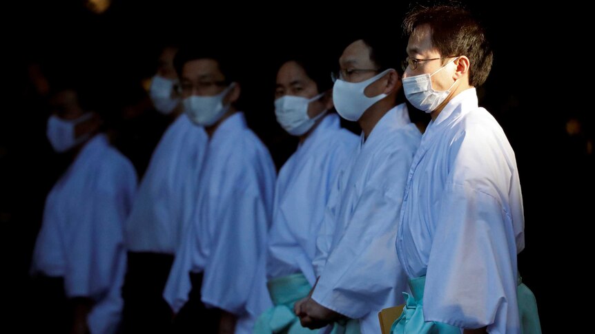 Men wearing white shirts and light blue wraps and medical masks.