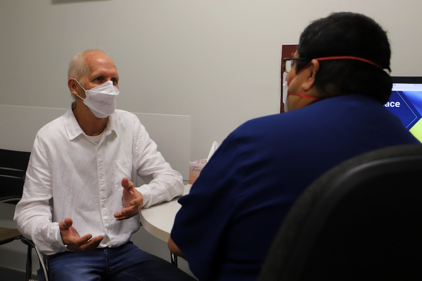 man in white shirt with mask talking to man in navy scrubs