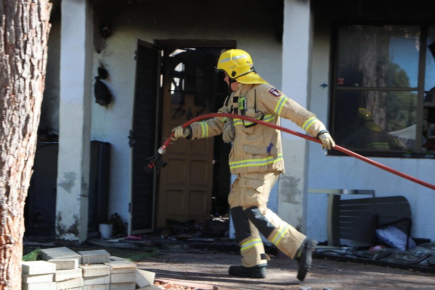 A firefighter walks carrying a fire hose outside a burnt-out house.