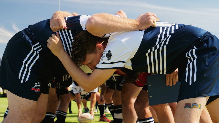 A group of men locked arms in a rugby scrum with a ball being knocked through the scrum by their feet.