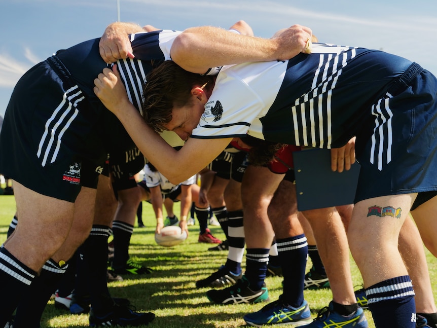 A group of men locked arms in a rugby scrum with a ball being knocked through the scrum by their feet.