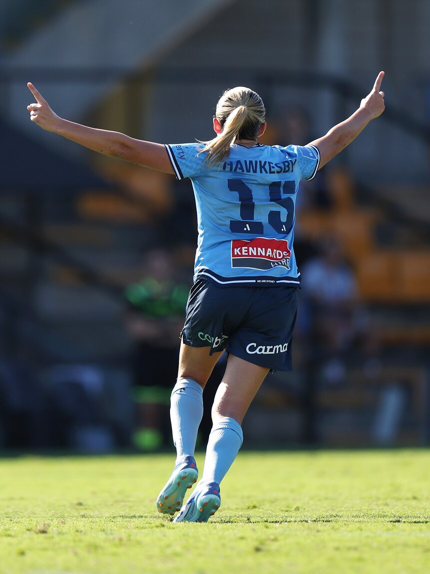 A soccer player wearing light blue puts her arms in the air during a game