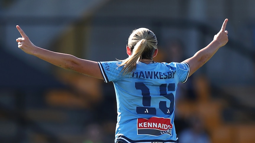 A soccer player wearing light blue puts her arms in the air during a game