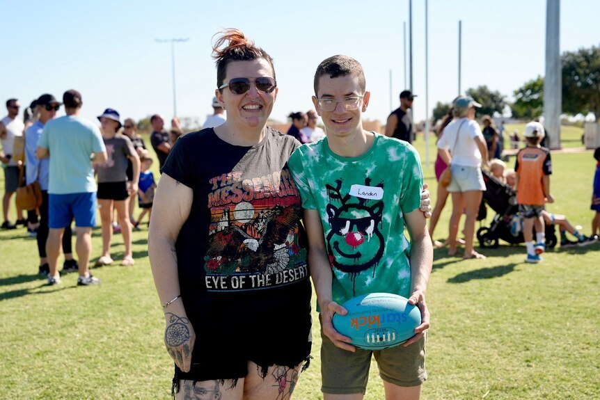 Woman standing next to her son, smiling, holding a football.