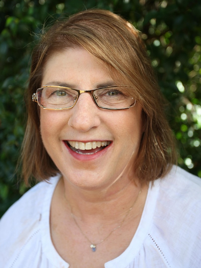 A smiling, dark haired woman wearing spectacles.