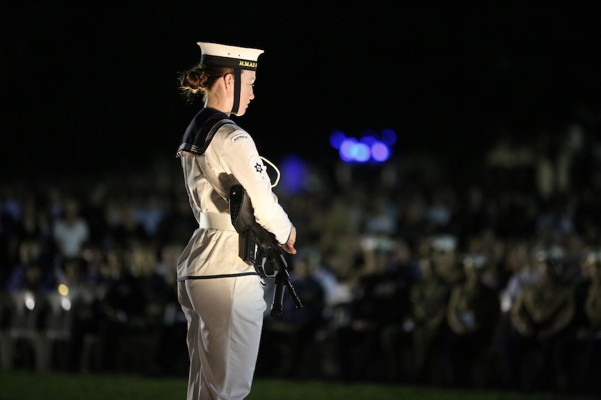 A woman in white navy uniform holds a rifle.
