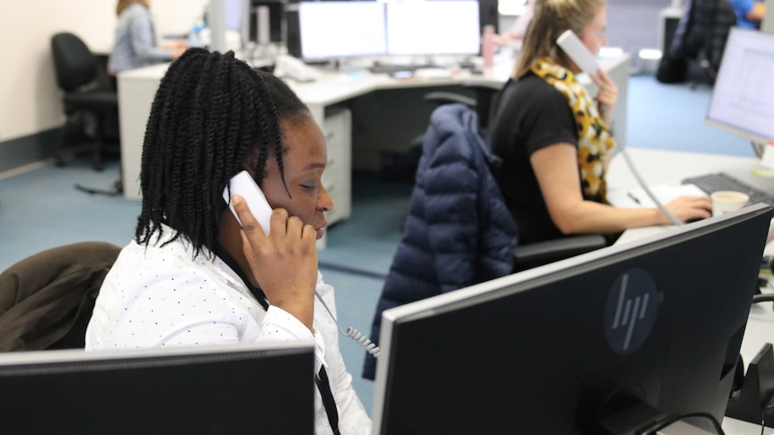 A woman at a desk takes a phone call and looks at a computer monitor.