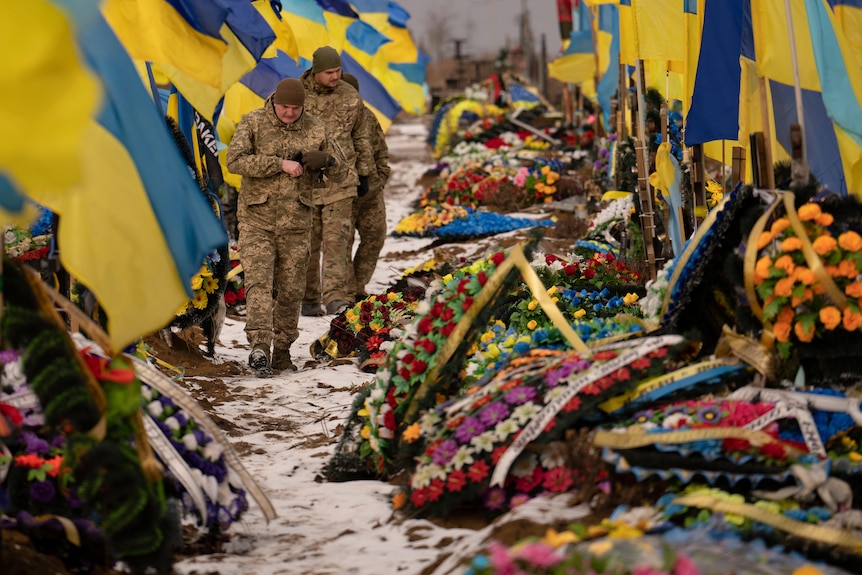 Ukrainian soldiers walk by the graves of fellow soldiers decorated with flags and flowers.