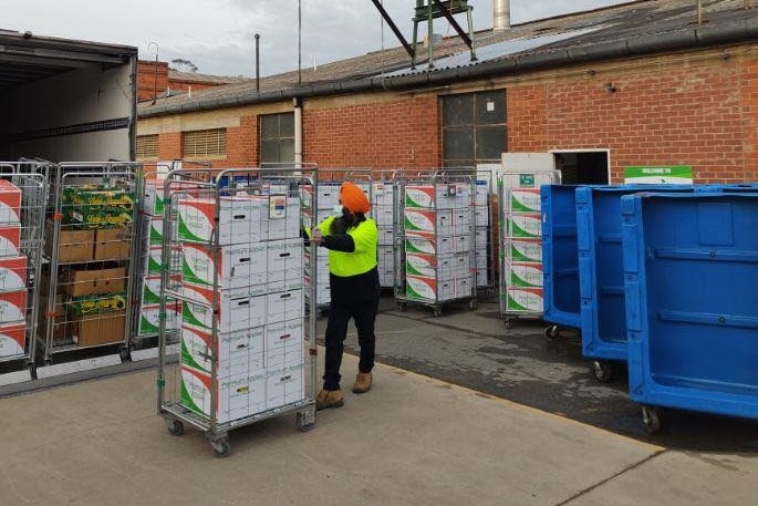 A man wheels a trolley full of boxes to a truck