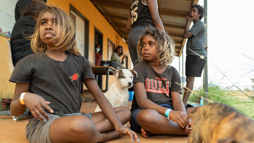 Children and a dog sit on the veranda of a house