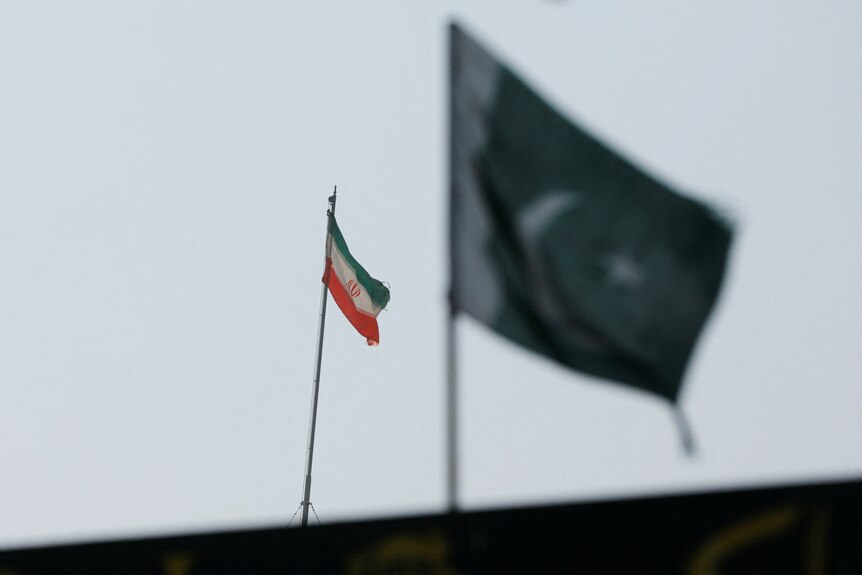 A Iranian flag flying in the foreground of a Pakistani flag 