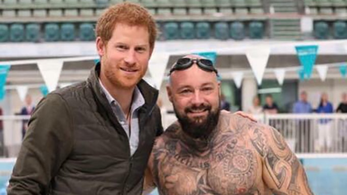 Prince Harry with Invictus Games athlete Tyrone Gawthorne stand together next to a pool.
