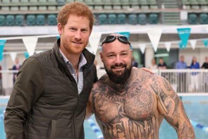 Prince Harry with Invictus Games athlete Tyrone Gawthorne stand together next to a pool.