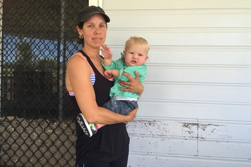 Catrina Stevens, with her son Theo, outside her Biloela home that was flooded by the Callide Dam