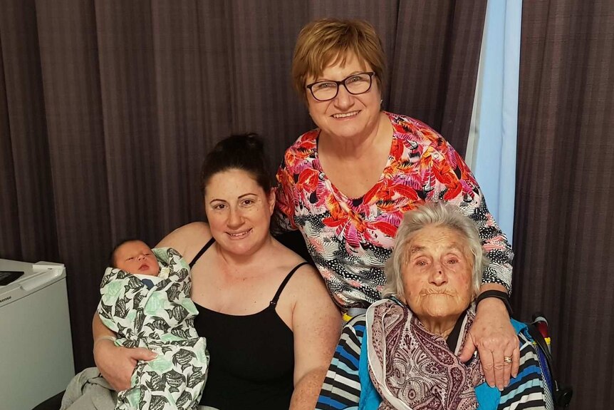 Four generations of family smiling at the camera.