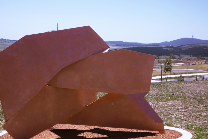 A large rust coloured sculpture sitting in a new housing development. 