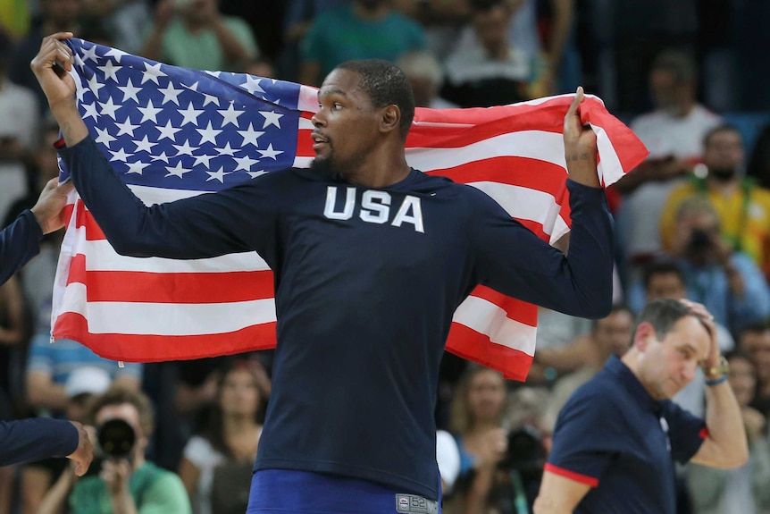 Kevin Durant looks to his right as he holds the United States flag behind his back during a basketball game