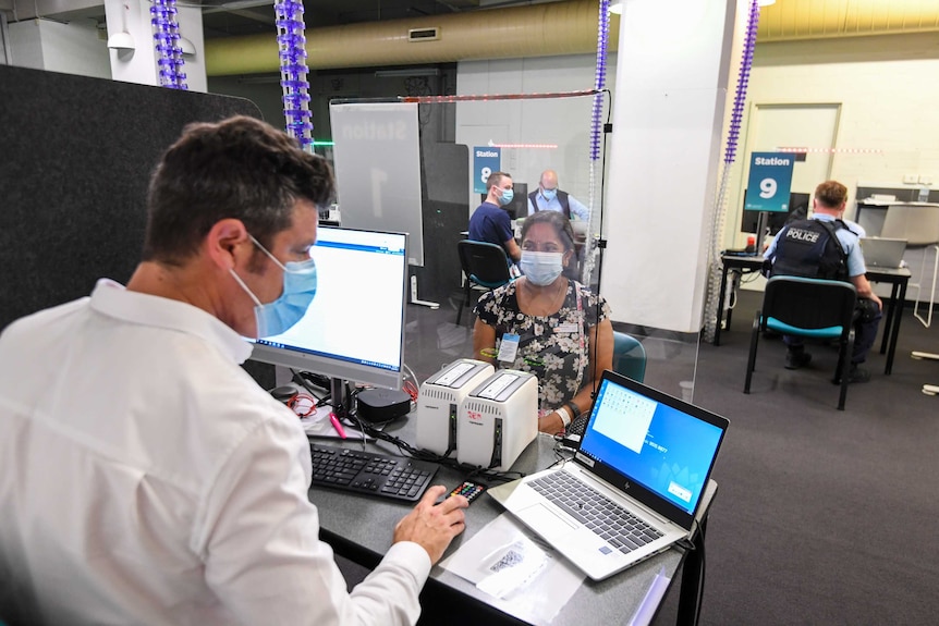 A man with a mask at a desk with a woman with a mask on the other side