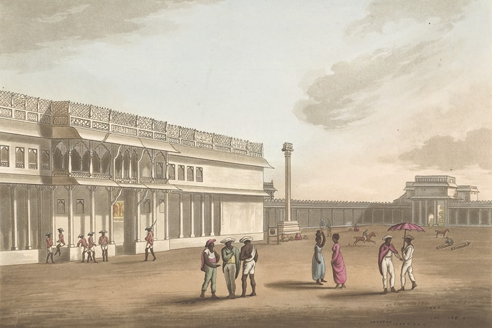 People and soldiers stand around in a square outside a palace. The palace is a two storied white building.