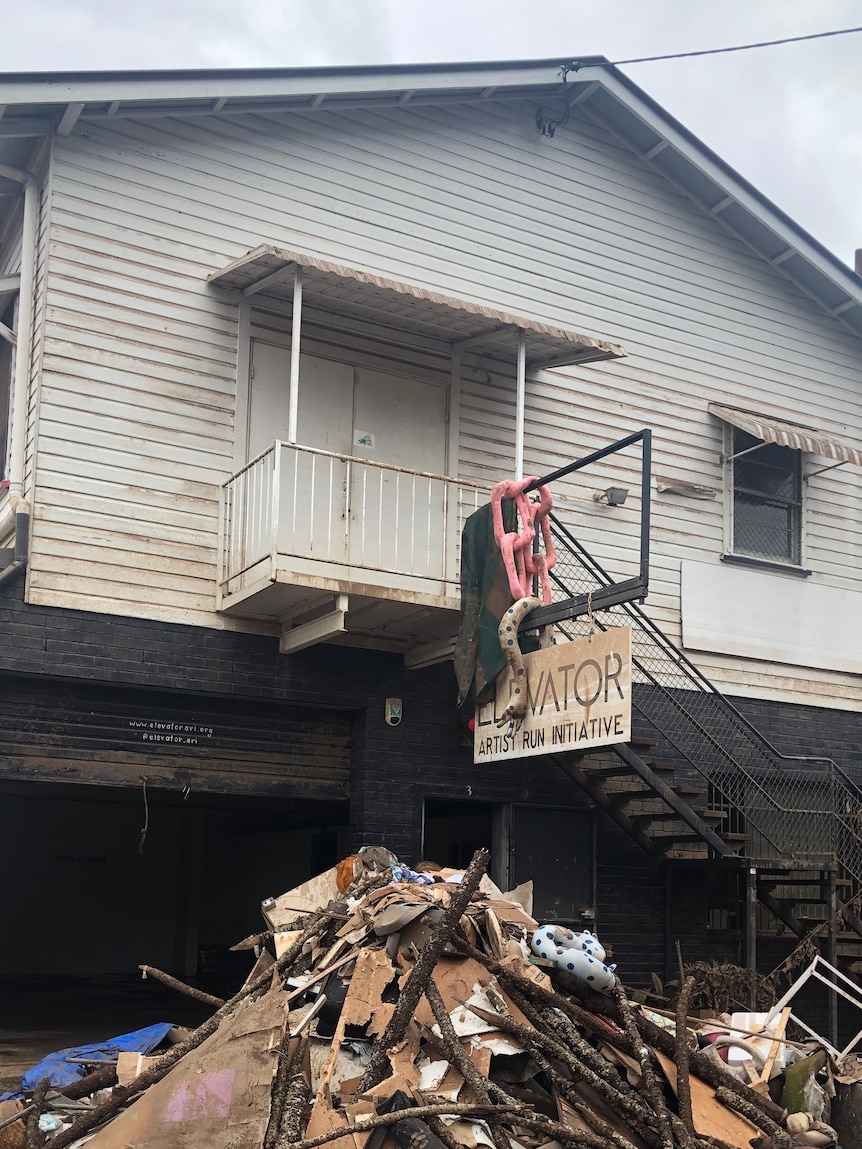 A pile of debris is piled high on a wet city street, below a building, with a sign that reads "ELEVATOR ARTIST RUN INITIATIVE"