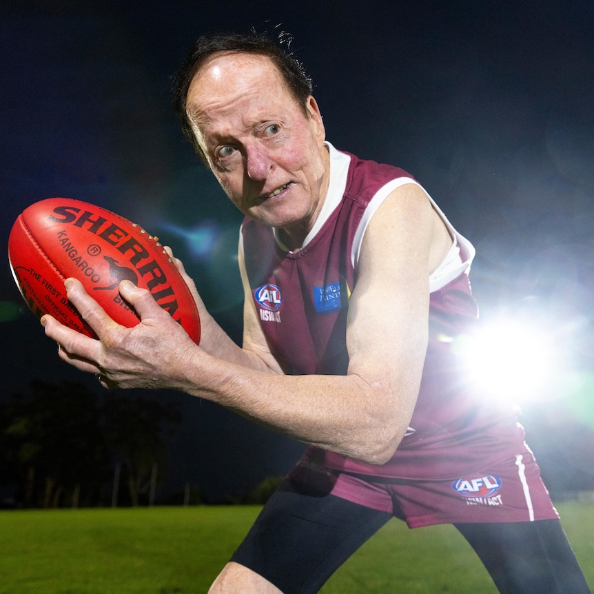 A man in a maroon Aussie Rules jersey holds a football at night