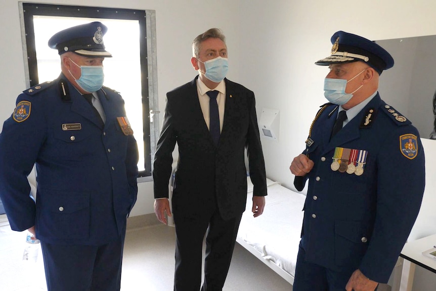 Two uniformed senior corrections officers and a suited politician in a prison cell