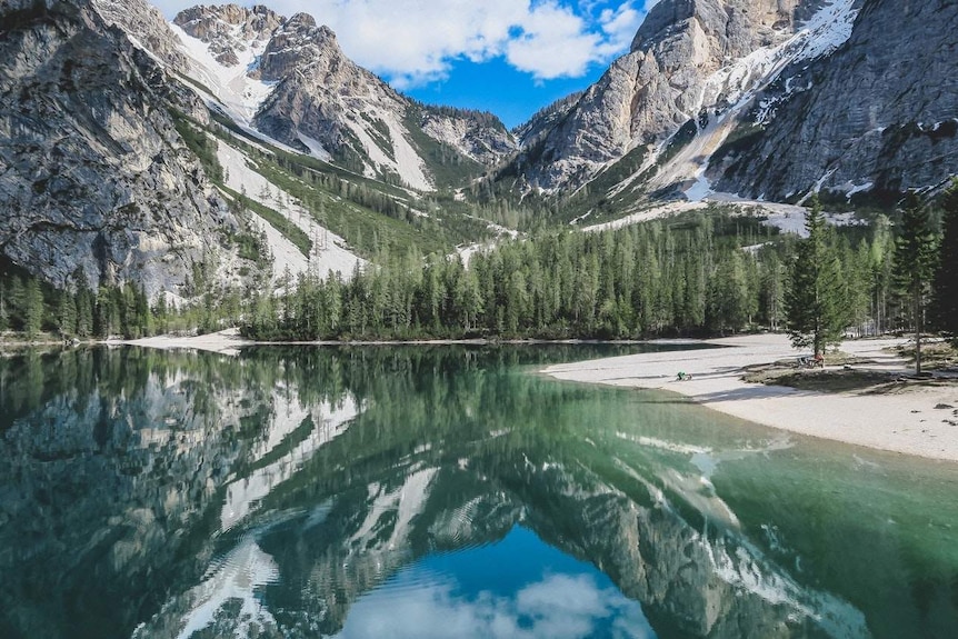 Snow-capped mountains are reflected in a lake in Italy.