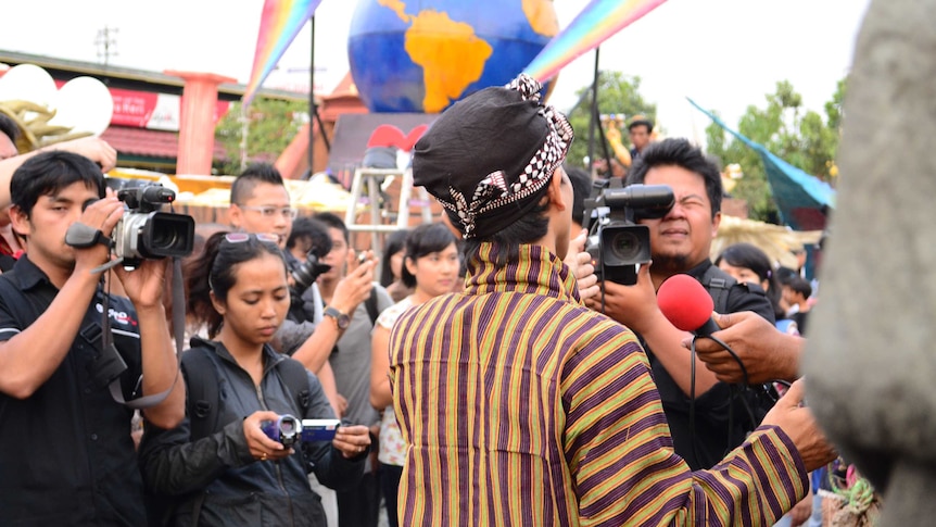 A man in Indonesian traditional outfit surrounded by journalists