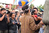 A man in Indonesian traditional outfit surrounded by journalists