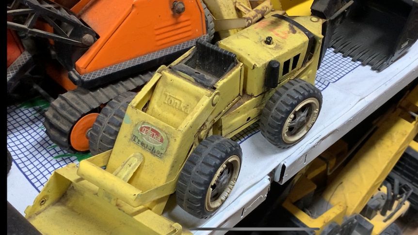A yellow worn looking toy excavator sits on a shelf