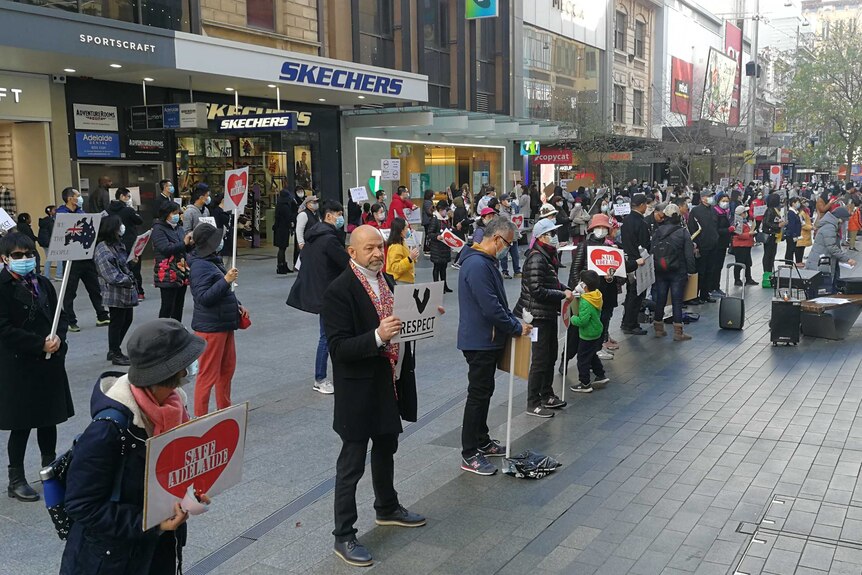 Protesters hold signs saying 'Safe Adelaide' and 'Respect' while standing around 1.5 metres apart in Adelaide.