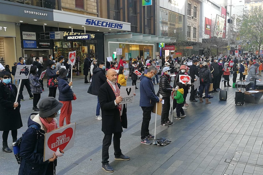 Protesters hold signs saying 'Safe Adelaide' and 'Respect' while standing around 1.5 metres apart in Adelaide.