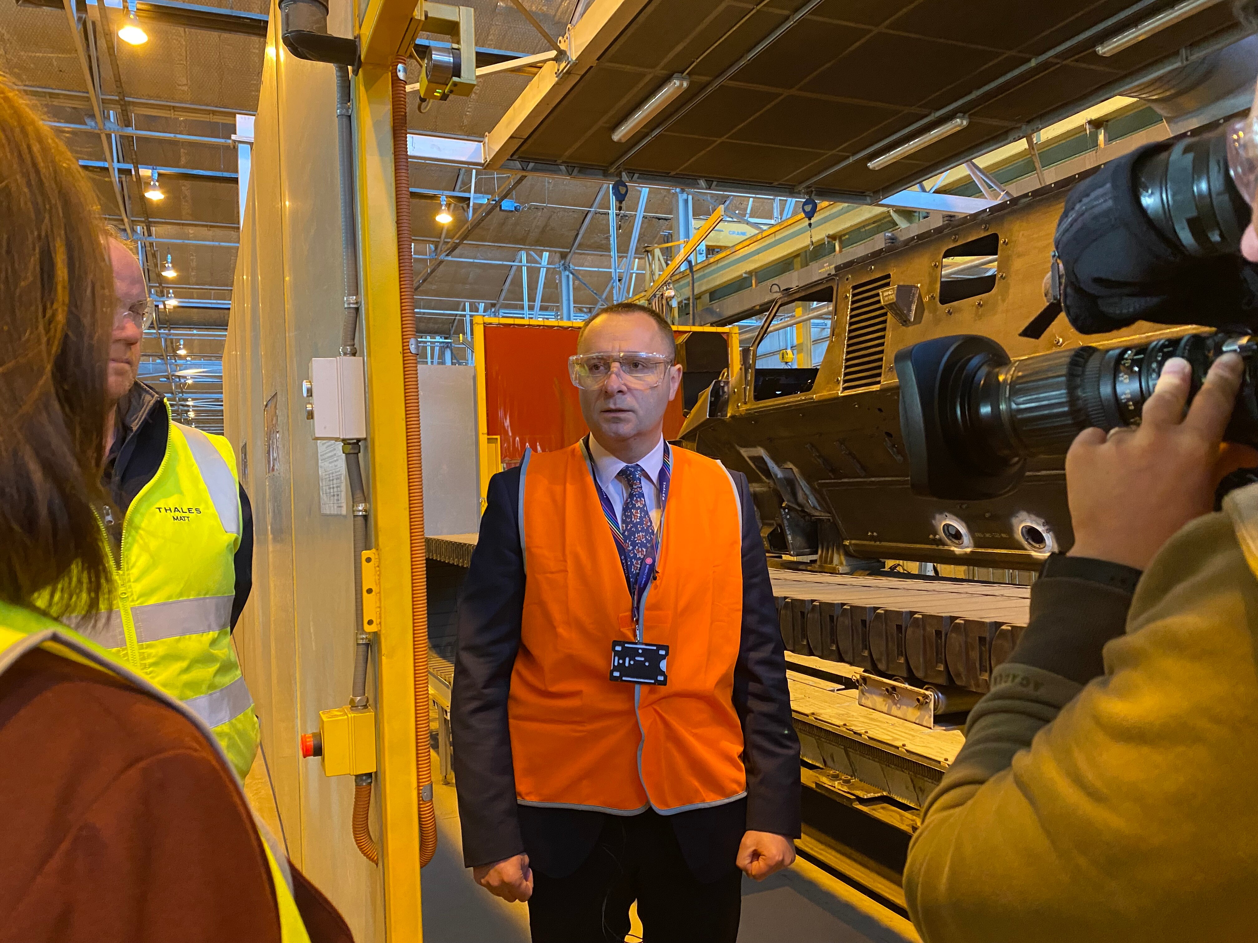 A man in a hi-vis vest stands inside a factory.
