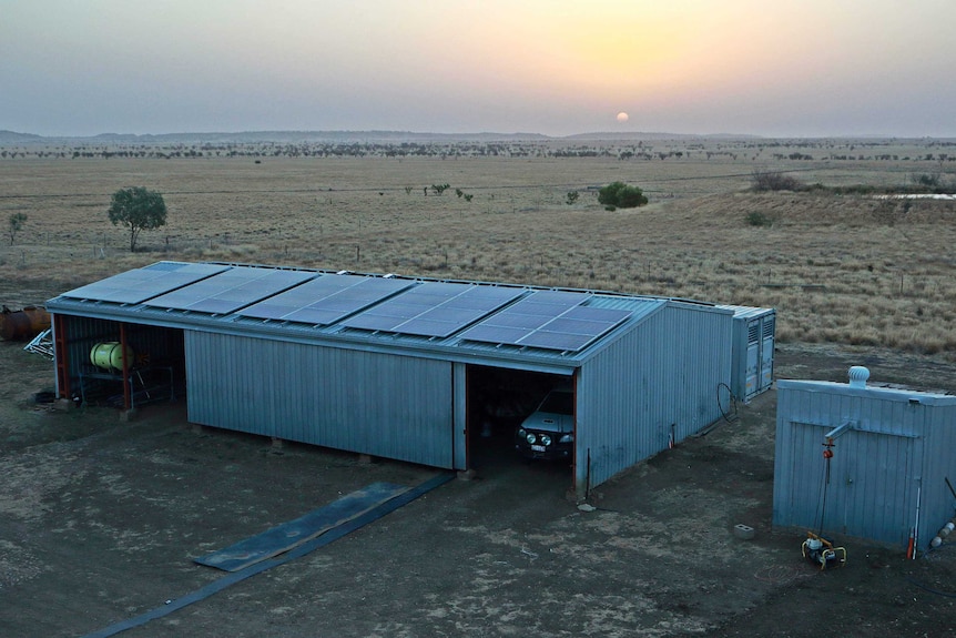 Aerial shot of solar panels on the roof of a shed at a cattle property at sunset