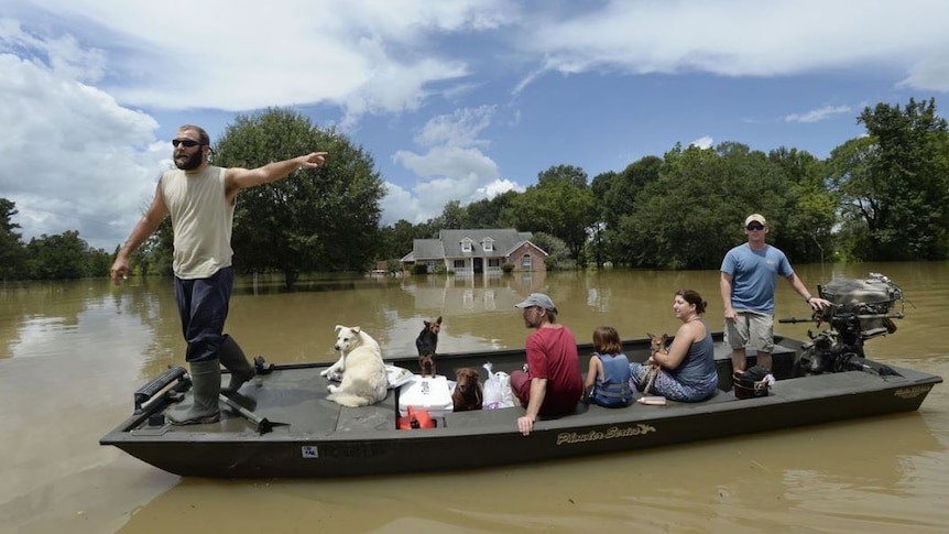 Two men move a family and their dogs in a flat-bottomed boat across floodwaters.