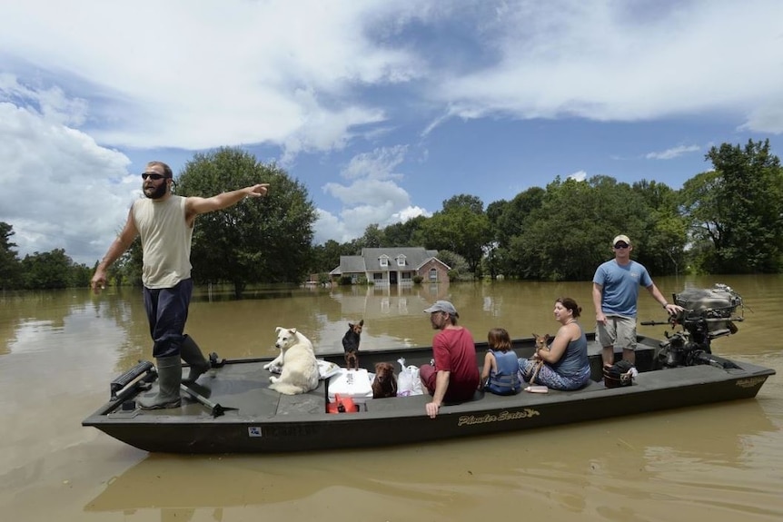 Two men move a family and their dogs in a flat-bottomed boat across floodwaters.