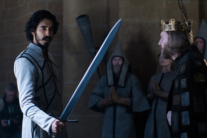 Young man with dark hair and beard wears white tunic with black trim and wields sword next to older man with gold crown.