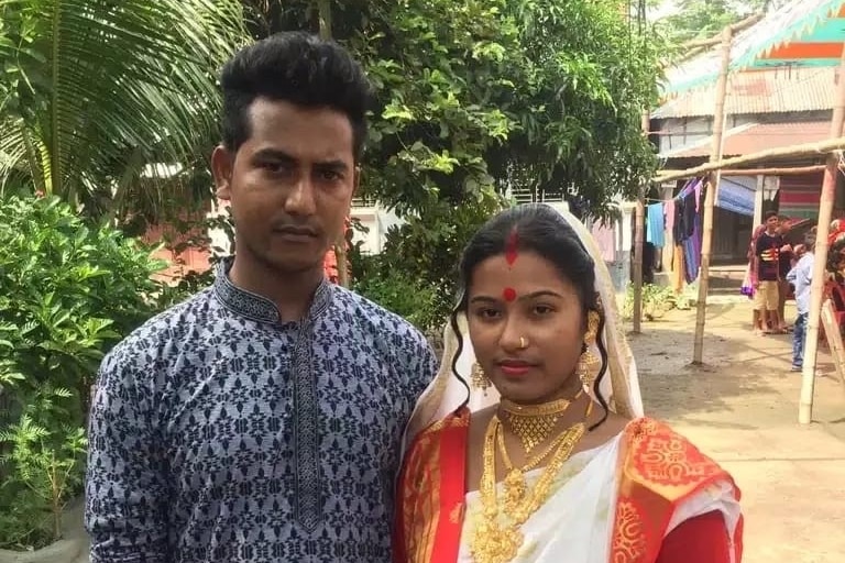 A young south Indian man in blue stands next to a young female in orange, white and red traditional garb.