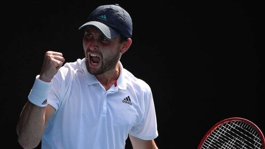 A cap-wearing tennis player pumps his fist in celebration during an Australian Open match.