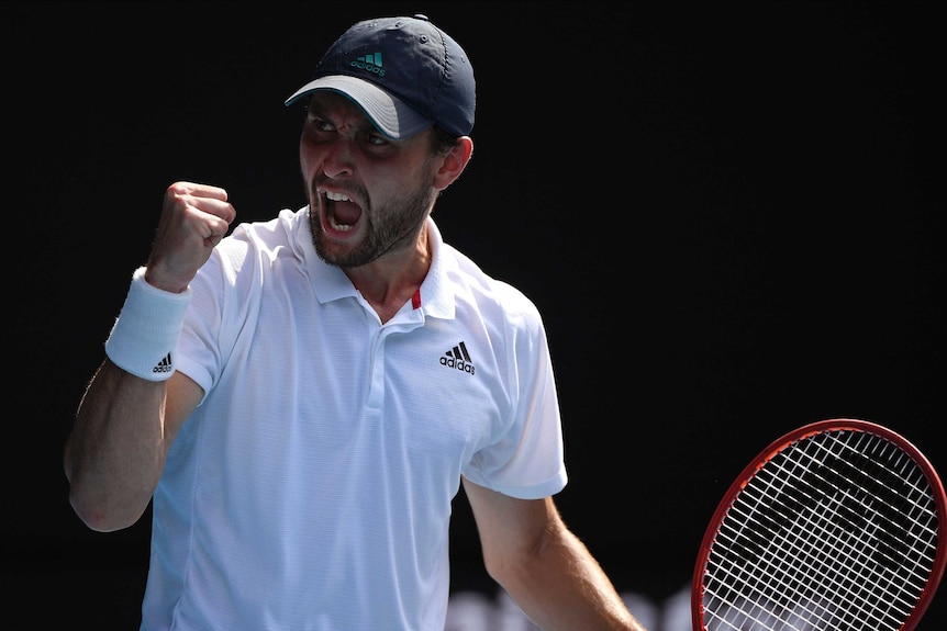 A cap-wearing tennis player pumps his fist in celebration during an Australian Open match.