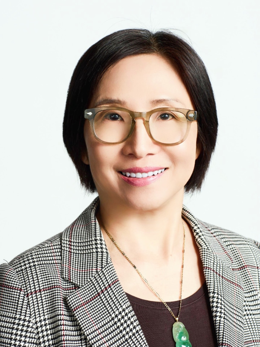 A woman with black hair, glasses and a blazer smiling for the camera