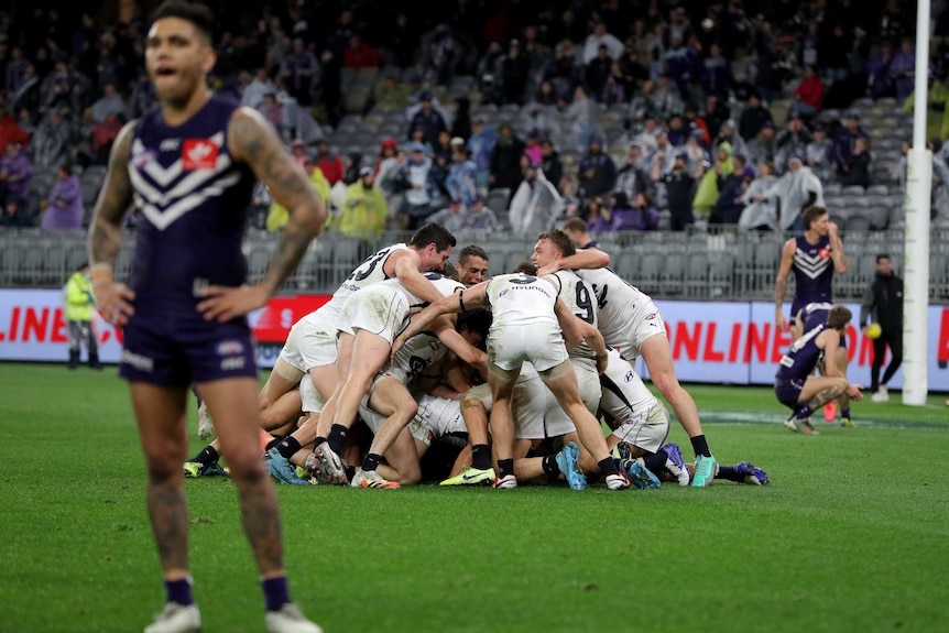 Carlton players pile on top of each other on the field as Fremantle players stand nearby