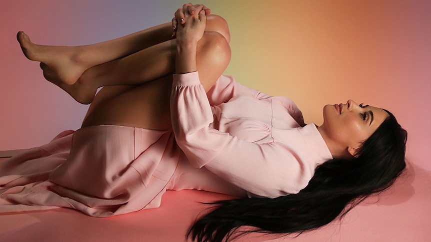 Kacey Musgraves lying on the ground against a rainbow backdrop
