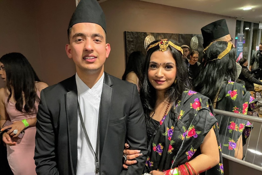 A man and woman in traditional Nepalese dress smile for the camera.